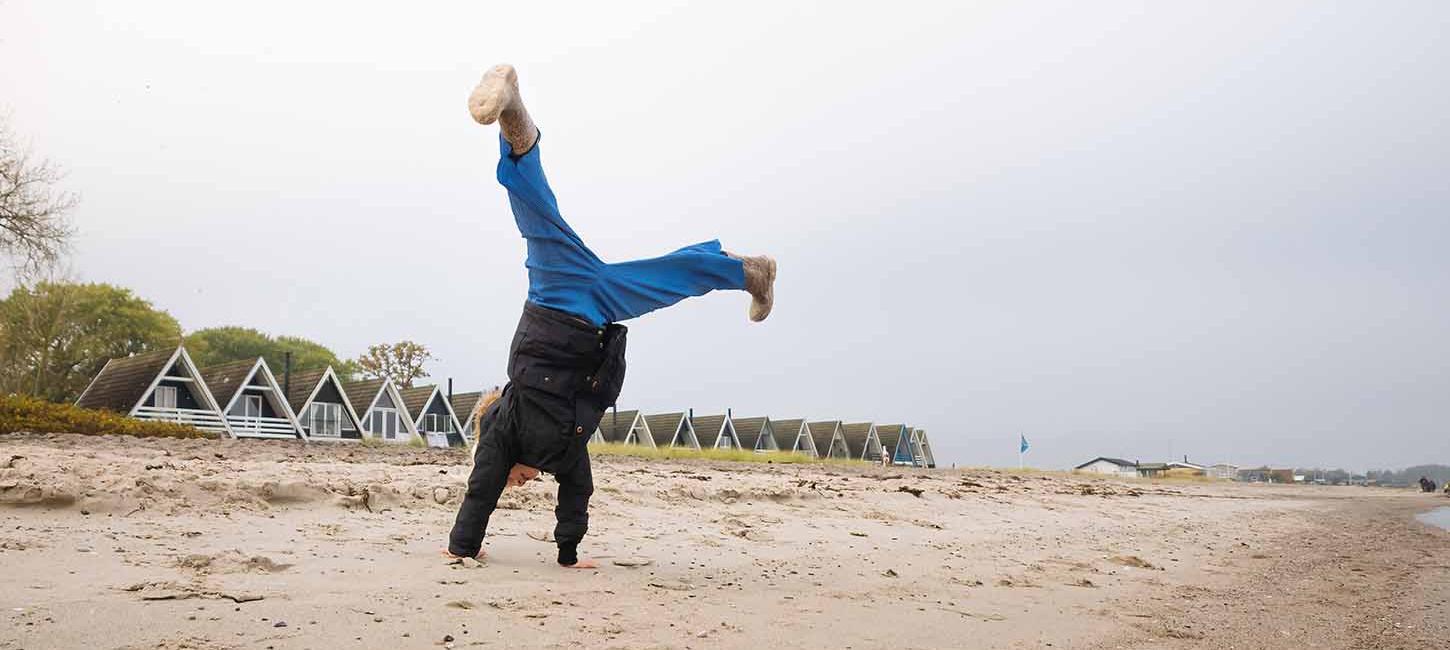 Barn slår vejrmøller på Hasmark Strand i efteråret med sommerhuse i baggrunden